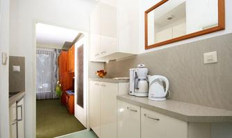 A modern kitchen with white cabinets and a countertop. On the countertop, there is a kettle and a bowl of fruit.