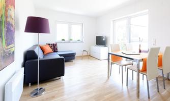 A bright living room with a modern sofa and a dining table. Large windows provide plenty of daylight and a cozy atmosphere.