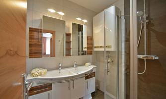 A modern bathroom with a shower cabin and an elegant sink. The walls are tiled in light colors, and there are large mirrors for added comfort.