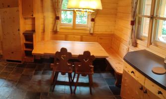 A cozy wooden kitchen with a dining table and two chairs. Large windows let in a lot of light.