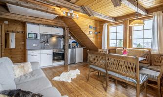 A cozy apartment with wooden details and large windows. The space is equipped with a modern kitchen and a dining area.