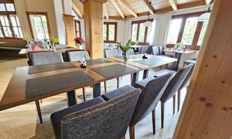 A modern restaurant with wooden details and large windows. The tables are set and decorated with flowers.