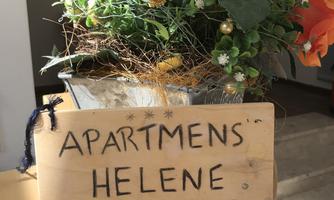 A sign with the inscription "Apartments Helene" stands next to a blooming plant. In the background, a bright room can be seen.