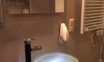 A modern bathroom with a stylish glass sink and an elegant faucet. The walls are brightly tiled, and there is a towel warmer.