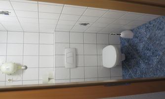 A small toilet with white tiles and a white toilet. The floor is tiled with blue tiles and there is a toilet brush holder.