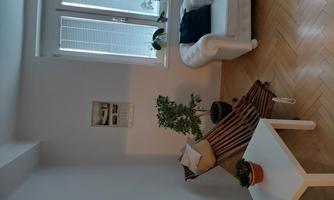 A cozy living space with a simple white sofa and a chaise lounge. Additionally, there are plants and a small table.