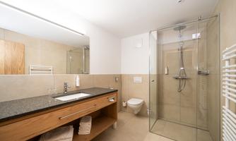 A modern bathroom with a glass shower cubicle and a wooden washbasin. The walls are bright and the furnishings appear clean and elegant.