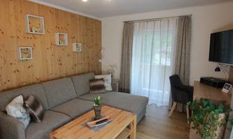 A cozy living room with a gray sofa and a wooden table. Large windows let in plenty of light and there are matching decorative elements.
