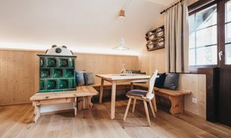 A cozy dining area with wooden paneling and an adjacent bench. The table is simple and modern, surrounded by chairs and a green box.