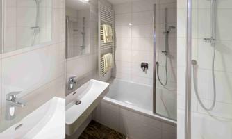A modern bathroom with a bathtub and a walk-in shower. White tiles and an elegant sink complete the design.