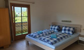 A cozy bedroom with a large bed and colorful pillows. The view through the window shows a green landscape.