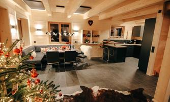A modern living room with wooden paneling and a cozy dining area. The room is festively decorated with a Christmas tree and warm light.