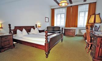 A cozy bedroom with a large double bed and a comfortable armchair. The windows let in plenty of light and are decorated with long, orange curtains.