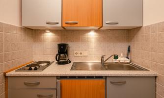 A small kitchen with gray and wooden cabinets. It is equipped with a stove, a coffee maker, and a sink.