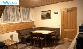 A cozy room with a dining table and benches. The walls are made of wood, and there is a picture as well as a large window area.