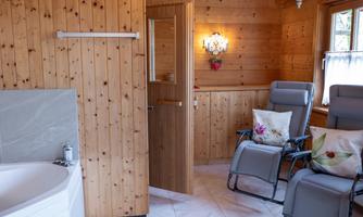 A cozy wellness area with wooden walls and comfortable lounge chairs. A whirlpool and gentle lighting create a relaxing atmosphere.