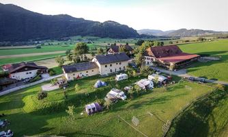 A picturesque farm in a green landscape, surrounded by gentle hills. Tents and campers are set up on the grounds, ideal for a holiday in nature.