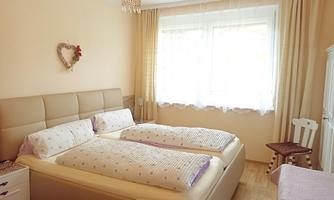 A bright bedroom with two beds and a large window. The walls are painted in soft colors and the decor is cozy.
