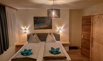 A cozy bedroom with a double bed and modern wooden decor. The walls are painted in warm tones, and a pretty lamp provides pleasant lighting.