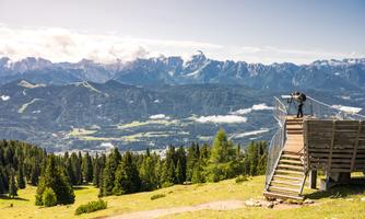 A breathtaking view of the mountains and the valley. A person is standing on an observation platform and enjoying the scenery.