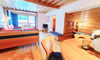 A cozy living space with a wooden ceiling and warm colors. The room features a sofa, a table, and plenty of natural light.