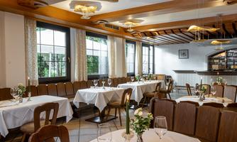 An elegant restaurant with white tablecloths and wooden chairs. The warm lights create a cozy atmosphere.