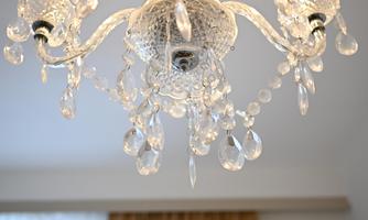 An elegant chandelier made of glass with many crystal accents. Curtains are visible in the background.