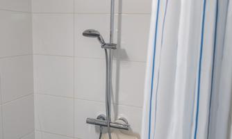 A modern shower with a large rainfall showerhead and a handheld showerhead. The walls are brightly tiled and a shower curtain with blue stripes is present.
