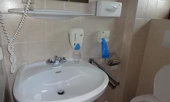 A clean bathroom with a sink, a mirror, and a toilet. On the wall, soap dispensers and towels are visible.