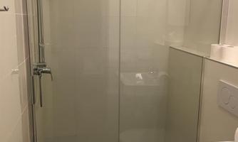 A modern shower with a glass partition in a bright bathroom. The bathroom features light tiles and an elegant sanitary installation.