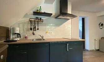 A modern kitchen with black cabinets and a light countertop. In the background, a coffee machine and various kitchen utensils are visible.