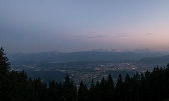 A breathtaking view of a city in the valley, surrounded by mountains and forests. The sky displays the soft colors of twilight.