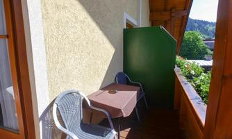 A small balcony with a table and two chairs. The surroundings are green and sunny.