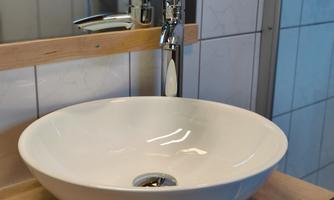 A modern sink made of white ceramic on a wooden surface. The faucet has an elegant, shiny design.