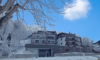 A modern building in a snowy landscape. The sky is clear and blue, surrounded by snow-covered trees.