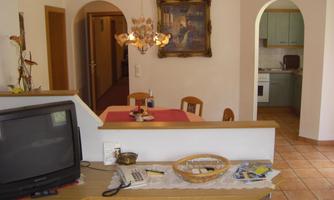 A cozy living area with a table and chairs. In the background, you can see a modern kitchen and an entrance area.