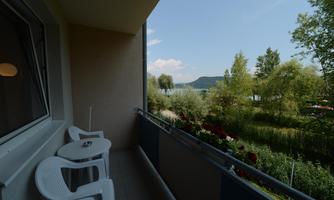 A balcony with two white chairs and a table. In the background, there are trees and a lake.