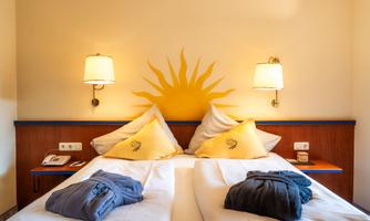 A cozy hotel room with a double bed and sun decorations on the wall. The room has large windows with a view of nature.