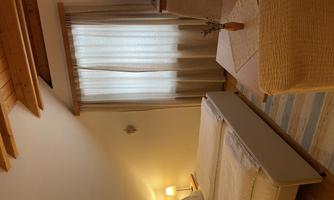 A cozy room with a bed, a television, and a small table. Soft curtains let the daylight in.