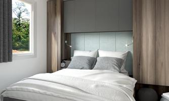 A modern bedroom with a comfortable double bed and gray accents. The window offers a view of a green surroundings.