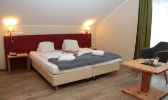 A cozy bedroom with a large bed and modern furnishings. There is a small table and an armchair, as well as soft light from the wall lamps.