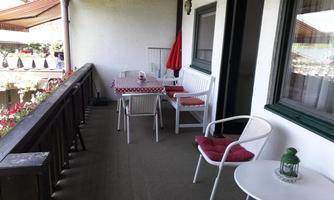 A cozy balcony with a table and chairs. Colorful flowers adorn the area and a beautiful view of the surroundings is visible.