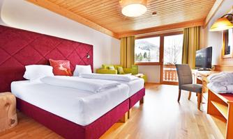 A modern hotel room with two single beds and a cozy seating area. Large windows offer a view of nature and plenty of natural light.