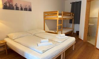A bright room with a double bed and a bunk bed. The walls are cheerfully designed, and there is access to a bathroom.