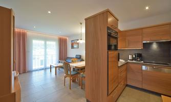 A modern kitchen with wooden cabinets and a dining area. There is plenty of natural light and a pleasant atmosphere.