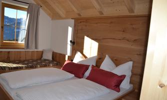 A cozy bedroom with a wooden ceiling and a large window. Two beds are decorated with white and red pillows.