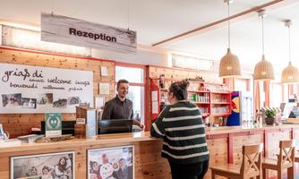 A friendly hotel reception with a smiling employee and an informed guest. The decor is made of wood and has a cozy atmosphere.