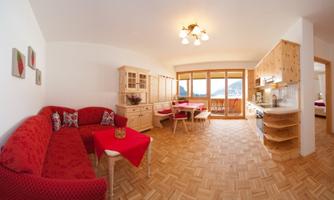 A cozy living space with a red sofa and wooden furniture. Large windows provide a beautiful view of the surroundings.