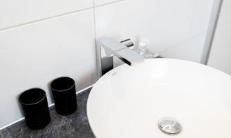 A modern sink with an elegant faucet. Next to the sink are two black cups.