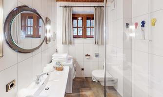 A modern bathroom with white tiles and wooden ceilings. There is a large mirror, fresh towels, and a shower with a glass door.